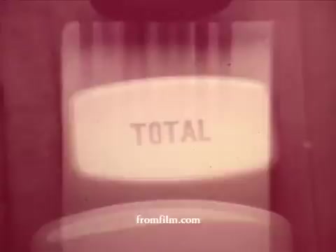 The still from the 'Chatham Supermarket Commercials' features a vintage 16mm cinematic aesthetic. The focus is on a display that shows the word 'TOTAL,' likely indicating a checkout or summary of purchases. Surrounding themes include common supermarket items such as apples, bananas, fresh cut meats, and potatoes, emphasizing the variety of goods available. The overall tone is nostalgic, showcasing a simpler, traditional approach to grocery shopping.