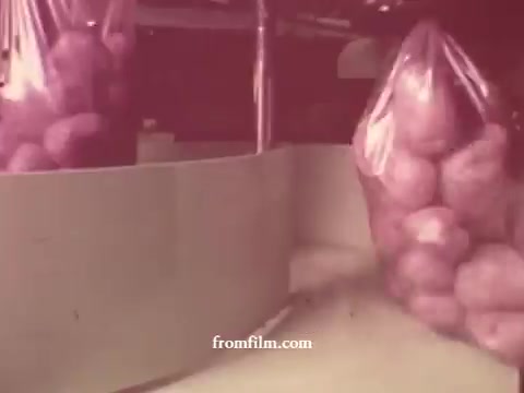 The 16mm still from the 'Chatham Supermarket Commercials' features a scene focused on bags of potatoes on display. The setting suggests a grocery store environment, highlighting fresh produce in a promotional context. The colors appear muted, a characteristic of older film stock, and the overall composition emphasizes the grocery items, potentially showcasing their appeal to customers.