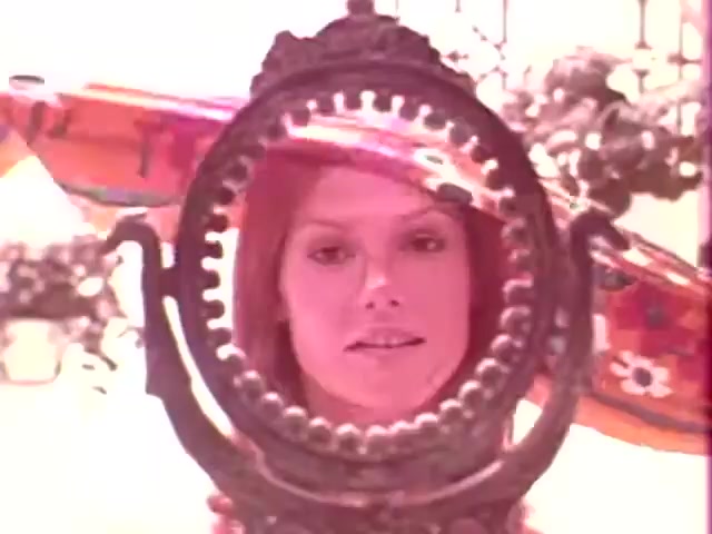 The still from 'Kleenex Boutique Tissues - 1970s' depicts a woman framed by an ornate mirror. Her expression is calm, and she appears to be in a soft, pastel-colored environment that evokes a vintage aesthetic typical of the 1970s. The composition highlights both the subject and the decorative elements surrounding her, suggesting a blend of beauty and elegance associated with the product being advertised.