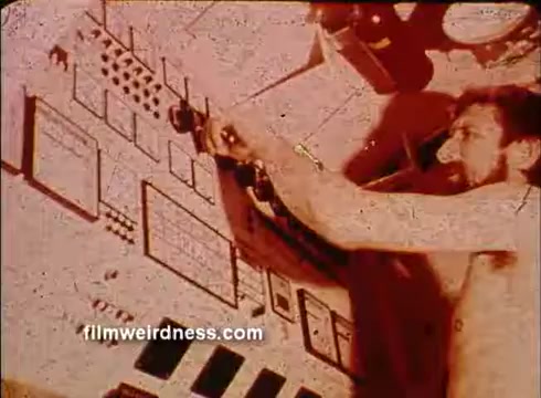 The still from the 'Helgoland fisheries research sponsorship/PSA' depicts a man operating a complex control panel with various buttons and screens. He appears focused, with his right hand engaged in adjusting one of the controls. The setting has a warm, reddish hue, suggesting an older film style. The scene emphasizes a scientific or research environment related to fisheries.