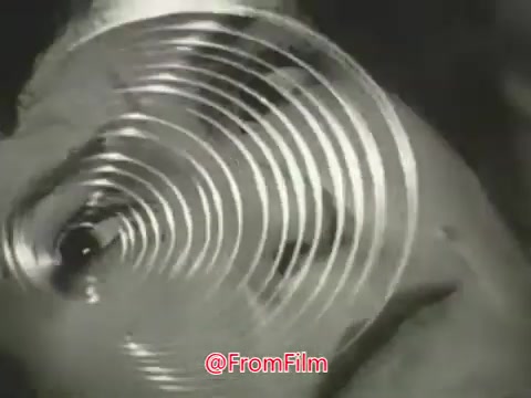 The still from the 'Sleep-eze' commercial features a close-up of a spiral pattern, likely a visual metaphor for relaxation or hypnotic effects associated with the product. The film's black-and-white style emphasizes a vintage aesthetic typical of the 1960s or 1970s, likely aiming to convey a calming or sleep-inducing message to the viewer.