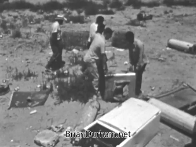 The still from the 'Volunteers in Service To America' PSA depicts a group of volunteers engaged in a community service project. They are seen working together to clean up a littered area, surrounded by discarded items. The scene illustrates the efforts of VISTA volunteers in addressing poverty and environmental challenges while promoting civic responsibility and community involvement during the 1960s.