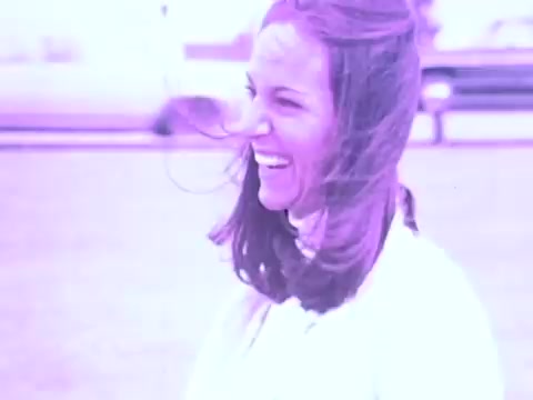 The still from the Gaines Burgers dog food commercial features a woman laughing joyfully, likely conveying a sense of happiness and connection with pets. The scene is characterized by a warm, nostalgic tone typical of 1970s advertisements. This playful engagement could suggest themes of companionship and the joy pets bring to families, aligning with the product's appeal. The visual style, with its distinctive color palette, reflects the era's aesthetic in advertising.