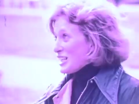 The still from the Gaines Burgers dog food commercial depicts a woman with light hair, smiling and engaging with someone off-camera. The image has a distinct purple tint, typical of the film quality from the 1970s. This advertisement likely aimed to highlight the appeal of Gaines Burgers, emphasizing a positive interaction related to pet care and dog food. The commercial was part of a campaign promoting the unique, patty-style format of the dog food, designed to look and feel like hamburger patties.