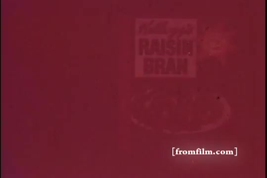 The still features a vintage advertisement for Kellogg's Raisin Bran, characteristic of 1970s style. The background has a faded quality typical of 16mm prints, emphasizing the retro aesthetic. The recognizable branding and logo of Raisin Bran are prominently displayed, along with a bowl of the cereal, suggesting a wholesome breakfast theme.