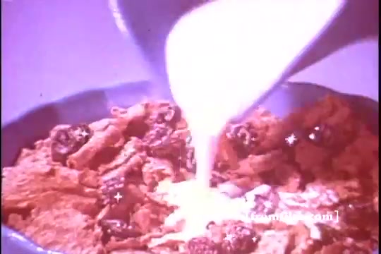 The still depicts a close-up of a bowl of Kellogg's Raisin Bran cereal with flakes and raisins visible. A stream of milk is being poured over the cereal, creating a dynamic and inviting visual. The colors are warm and slightly faded, typical of a 16mm print from the 1970s, evoking nostalgia for classic breakfast commercials.