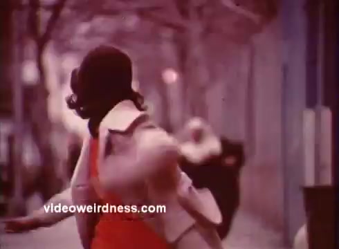 This still from *Come Back, Charleston Blue* captures a moment of urban life in the early 1970s, typical of the blaxploitation genre. The scene features a woman in a stylish coat, hinting at the fashion of the time. The soft color tone and background suggest a street setting, possibly invoking a sense of movement or urgency.   The film follows characters Coffin Ed Johnson and Grave Digger Jones as they navigate themes of crime and societal challenges. This still reflects the film's exploration of African American culture and community, aligned with the narratives found in Chester Himes' works. The use of fashion and setting establishes both character and context within the broader themes of the film.