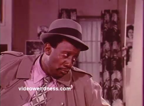 The 16mm still from *Come Back, Charleston Blue* features a character in a classic trench coat and fedora. The overall aesthetic reflects the blaxploitation genre, capturing the unique fashion and mood of the early '70s. The character's expression conveys a mix of intrigue and contemplation, fitting the film's themes of crime and social commentary. The backdrop suggests a domestic setting, which contrasts with the film's action and drama elements. This still embodies the essence of the film, contributing to its cult classic status.