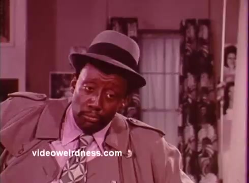 The still from 'Come Back, Charleston Blue' features a character in a stylish, classic blaxploitation attire, highlighted by a trench coat and a distinctive hat. Set in a vibrant 1970s environment, the character's expression conveys a sense of cool confidence, a common trait among the genre's protagonists. The film, which continues the story of Coffin Ed Johnson and Gravedigger Jones, blends crime, humor, and social commentary, reflecting the era's cultural dynamics and cinematic style. The use of color and composition adds to the film's iconic visual appeal.
