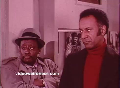 The 16mm still from 'Come Back, Charleston Blue' features two main characters: Coffin Ed Johnson and Gravedigger Jones, portrayed by Godfrey Cambridge and Raymond St. Jacques, respectively. The setting suggests a tense moment, possibly indicating an investigation or confrontation. The characters' expressions reflect a mix of seriousness and contemplation, characteristic of the blaxploitation genre. The film, a sequel to 'Cotton Comes to Harlem,' continues exploring themes of crime and social issues, while incorporating elements of humor and drama. Their attire and the film's color palette convey the 1970s aesthetic typical of that era's cinema.