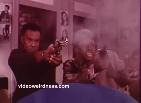 The still from 'Come Back, Charleston Blue' depicts two characters, Coffin Ed Johnson and Gravedigger Jones, engaged in a tense moment. Both men are holding guns, with expressions that suggest urgency or danger. Smoke fills the scene, likely from gunfire, creating a dramatic and intense atmosphere typical of the blaxploitation genre. The background hints at a stylized environment, contributing to the film's dynamic visual narrative. This film explores themes of crime and justice, reflecting the socio-political landscape of its time.