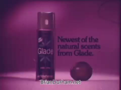 The still features a vintage advertisement for Glade, showcasing a spray can with a vibrant purple background. The text highlights it as the 'Newest of the natural scents from Glade,' emphasizing its freshness and appeal. A fruit, likely a lime, is positioned beside the can, reinforcing the scent theme. The overall aesthetic reflects 1960s commercial design, characterized by bold colors and playful graphics.