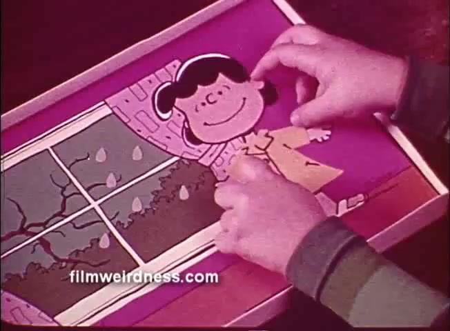 The still depicts a child’s interaction with a Colorforms set from 'How's The Weather, Lucy - Colorforms Peanuts'. It shows a window scene with Lucy, a character from the Peanuts comic strip, being placed on a colorful background. The scene outside features rain, emphasizing a weather theme. The hands of the child are actively positioning Lucy in her yellow raincoat, enhancing the playful, creative nature of the activity.