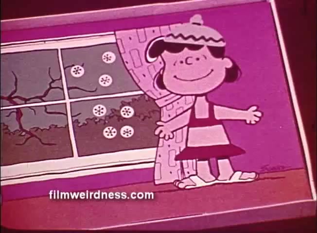 The still features Lucy from the Peanuts cartoon, smiling and wearing a striped dress and a hat. She stands in front of a window decorated with snowflakes, suggesting winter weather outside. The scene has a colorful, simplistic design typical of animation, emphasizing a cheerful atmosphere despite the cold setting.