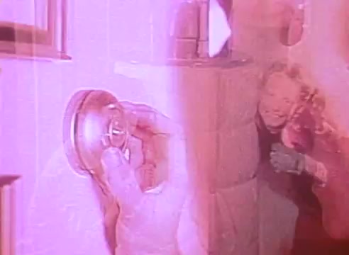 The still features an abstract, double-exposed image. On one side, a hand is shown adjusting a knob or mechanism, likely related to energy efficiency, while on the other side, a smiling person is seen, suggesting warmth and comfort. The color palette leans toward pinkish hues, evoking a hopeful and inviting atmosphere, reinforcing the theme of energy-efficient homes.