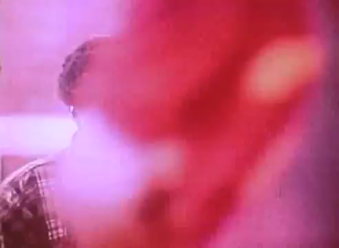 The still from 'Welcome to Fulton St - energy efficient houses PSA 2' features a blurry figure, possibly a person, partially obscured by a red object. The colors appear warm, with a soft focus that creates a dreamy or nostalgic atmosphere. The context suggests a focus on energy-efficient housing, possibly involving community or family interactions within a home setting.