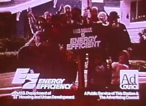 The still features a group of people gathered outdoors, smiling and holding a sign that proclaims 'This House is ENERGY EFFICIENT.' The visuals are connected to a public service announcement promoting energy efficiency in homes, with logos from the U.S. Department of Housing and Urban Development and the Ad Council. The backdrop suggests a residential setting, emphasizing community involvement in energy conservation.