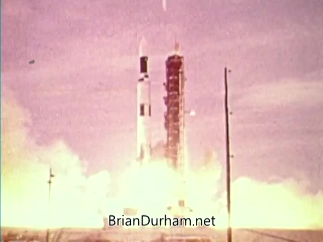 The still depicts a rocket launch, likely from a space program, with powerful flames and smoke erupting from the base as it ascends against a pastel sky. The scene captures the excitement and optimism of space exploration during the 1976 Bicentennial celebration, framed by the context of the PSA featuring James Whitmore. The image conveys a sense of progress and ambition in technology and exploration.