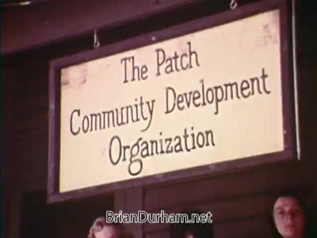 The still features a sign reading 'The Patch Community Development Organization,' likely highlighting a community initiative from the 1976 PSA 'Horizons On Display' with James Whitmore. The scene appears to be focused on community engagement and development efforts during the Bicentennial celebration.