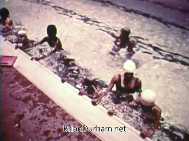The still from 'Horizons On Display - Bicentennial PSA' features children swimming in a pool, demonstrating water safety and recreation. Some children are wearing swim caps, and there are adults accompanying them, highlighting community engagement and the importance of swimming education. The scene reflects a sense of joy and activity, aligned with the PSA's positive message around the 1976 Bicentennial celebration.