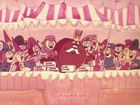 The still from the Hostess Ding Dong commercial features a vibrant animated scene set in a festive environment. A central character, likely a large, cartoonish figure, is adorned with a crown and a mustache, presumably representing the 'king' of Ding Dongs. Surrounding him are various whimsical characters, wearing colorful costumes, all joyfully celebrating and expressing excitement. The backdrop shows striped tents, enhancing the carnival-like atmosphere. The overall tone is cheerful and playful, typical of vintage commercials aimed at appealing to children.