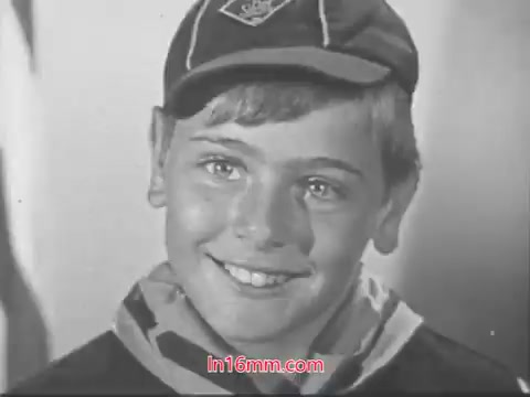 The still features a smiling young boy, likely a Cub Scout, wearing a cap adorned with the Cub Scouts logo. He has short, light brown hair and bright eyes, conveying enthusiasm and engagement. The background is likely simple, focusing on the boy's cheerful expression as he answers questions about his experiences in Cub Scouts, emphasizing fun activities such as flying kites, making things, and learning new skills. Overall, the image captures the positive spirit of youth and scouting.