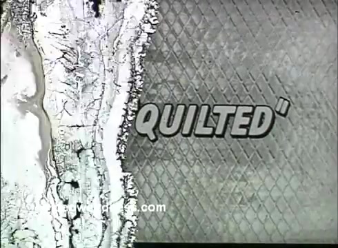 The still from the 16mm animated commercial 'It's Quilted' for Kaiser Aluminum Foil features the word 'QUILTED' prominently displayed in a bold, stylized font. The background shows a textured pattern that resembles a quilted surface, enhancing the theme of the product. The visual elements reflect the mid-1950s aesthetic, combining simple animation techniques with eye-catching graphics to highlight the uniqueness of the aluminum foil. The overall composition suggests a focus on quality and innovation.