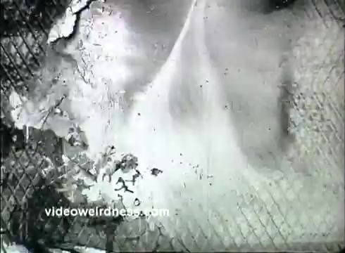 The still from the 16mm film 'Kaiser Aluminum - Pillsbury Bake Off 1957' depicts a textured surface, likely an aluminum kitchen item, with signs of wear and a sprinkle of flour or a white substance. The background features a grid-like pattern that suggests a baking or cooking theme, consistent with the context of a bake-off competition. The overall tone is monochromatic, enhancing the vintage feel of the print.