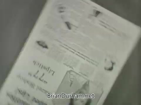 The still from the 16mm footage features a vintage advertisement for Hazel Bishop's 77 lipstick from the 1950s. The image likely depicts a printed promotional piece showcasing the product, highlighting its design and features, with text and graphics characteristic of the era's advertising style. The aesthetic reflects mid-20th century marketing techniques, appealing to consumers with a focus on beauty and cosmetics.