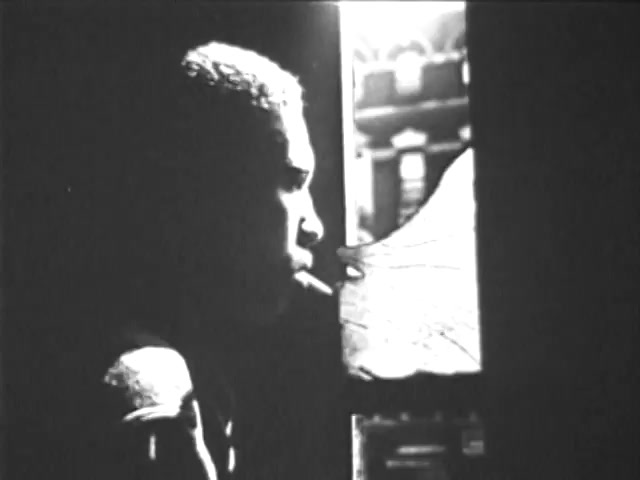 The still from the 'Ad Council PSA - Presidents Council on Youth Opportunity' depicts a young person in profile, seated beside an old-fashioned gramophone. The lighting creates a stark contrast, highlighting the figure's contemplative expression, while smoke from a cigarette adds to the moody atmosphere. The focus is on the interplay between the light and shadows, emphasizing themes of reflection and opportunity.