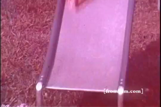 The still shows a close-up of a slide, likely in a backyard setting, with vibrant colors typical of 1970s film. A bag of Baggies Food Storage Bags is visible, possibly sliding down the incline, suggesting a playful or promotional context. The grassy area surrounding the slide adds to the nostalgic, playful atmosphere of the era.