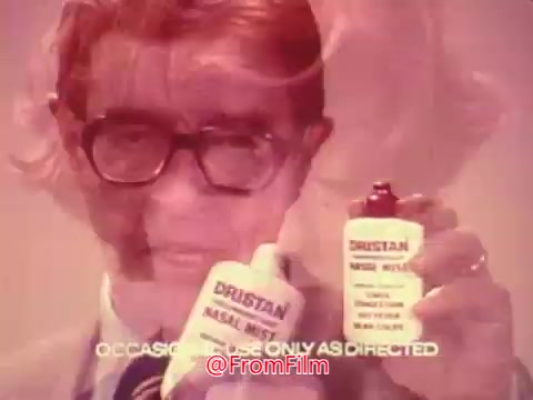 The still features a man with glasses holding two bottles of Dristan nasal spray, promoting the product. The colors are muted, typical of 1970s advertisements, with a soft-focus background. Text at the bottom reads “OCCASIONAL USE ONLY AS DIRECTED.” The overall aesthetic reflects the era's style in marketing health products.