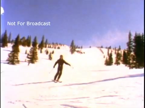 The still features a skier gliding down a snowy slope, surrounded by pine trees under a clear blue sky. The scene conveys a sense of winter recreation and the beauty of nature, fitting the context of a public service announcement featuring John Denver. The overlay text indicates it is not for broadcast.