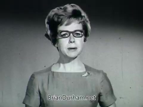 The still you've described from the 'Plantivater commercial - 'A Max Klein Product'' features a woman speaking directly to the camera. She appears confident but expresses concern about her ability to care for plants, stating, 'I don't have a green thumb. I'm not very good with plants.' The voiceover reassures her with 'Madam. With Plant.'  The setting seems to be a simple background, emphasizing the woman's appearance and the message of the commercial. She's dressed in a classic, perhaps vintage, outfit that reflects the advertising styles of the era, likely aimed at promoting the Plantivater planters as a solution for plant care. The use of black and white film adds a nostalgic feel to the visual, reminiscent of mid-20th century