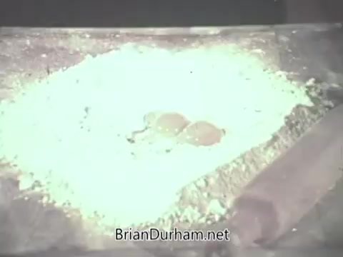 The still from the 'Pennsylvania Dutch Egg Noodle Commercial' features a close-up of a surface covered in flour. In the center, two eggs are placed atop the flour, suggesting the beginning of a cooking process. The scene likely evokes a homemade, traditional approach to making egg noodles, emphasizing freshness and authenticity characteristic of the Pennsylvania Dutch culinary style. The lighting and composition reflect a nostalgic, vintage aesthetic typical of commercials from the 1960s.