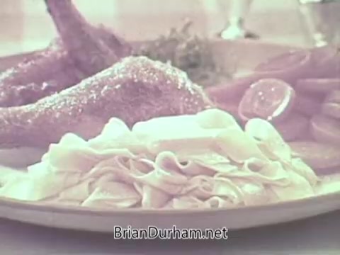 The still features a plate displaying Pennsylvania Dutch egg noodles accompanied by roasted chicken legs and slices of lemon. The scene emphasizes a home-cooked, hearty meal, highlighting the texture and appearance of the noodles as a key component. The warm color tones suggest a nostalgic, inviting atmosphere typical of 1960s food commercials.