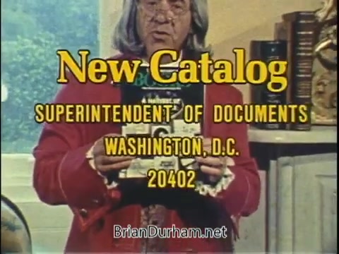 The still from 'US Government PSA - New Catalog' features a speaker holding a document titled 'New Catalog.' The text prominently displays 'SUPERINTENDENT OF DOCUMENTS' along with the address 'WASHINGTON, D.C. 20402.' The setting appears to be a well-lit room, possibly an office, with a decorative background. The overall tone suggests an informative and official presentation related to government documents.
