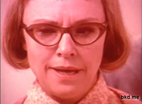 The still features a woman with short, styled hair and large glasses, wearing a patterned blouse and a serious expression. The colors appear somewhat washed out, typical of 1970s film prints, giving the image a nostalgic and vintage feel. The context suggests she is likely promoting or discussing the benefits of Spic and Span cleaning products.