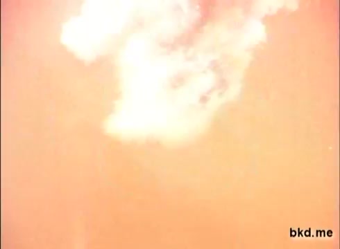 The still from the 1970s 'Spic and Span' commercial features a bright, hazy background with white cloud-like formations. The image has a warm tone, indicative of the era's film quality, creating a nostalgic feel. The composition suggests a focus on vibrant visuals that may relate to cleaning or freshness, aligning with the product’s branding.