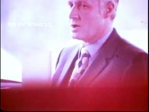 The still features a man in a suit, likely delivering a message or speech related to the Job Corps program. The color palette appears faded, typical of 1970s film, with a reddish tint. The background is blurred, focusing attention on the speaker, who conveys a sense of authority and purpose. The phrase 'Not For Broadcast' indicates this is an archival or private piece.