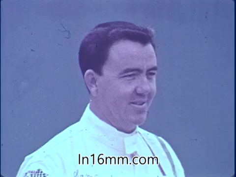 The still features Sam McQuaig, a professional stock car driver, likely captured in a moment reflecting confidence and expertise. He is wearing a racing suit, which emphasizes his connection to the sport. The background appears blurred, focusing attention on him and suggesting a racing environment. This context aligns with his message about the importance of safety equipment following a crash at Darlington Raceway.