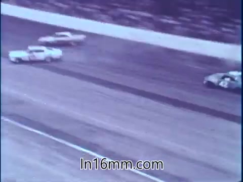 The still from the PSA features a racing scene at Darlington Raceway, showcasing multiple stock cars speeding around the track. The image captures a moment of high-speed action, emphasizing the competitive nature of racing. Sam McQuaig, as a professional driver, highlights the importance of safety equipment during such unpredictable situations. The context suggests a focus on safety awareness in racing, particularly following the dramatic events of the Southern 500.