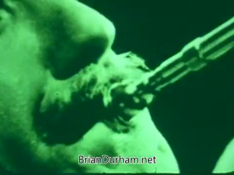 The still from 'Pittsburgh Symphony Promenades Commercial' features a close-up of a musician playing a brass instrument. The image is heavily tinted in green, highlighting the musician's concentration and the detail of the instrument. The focus on the mouthpiece suggests a dynamic moment in performance, capturing the intensity of live music.