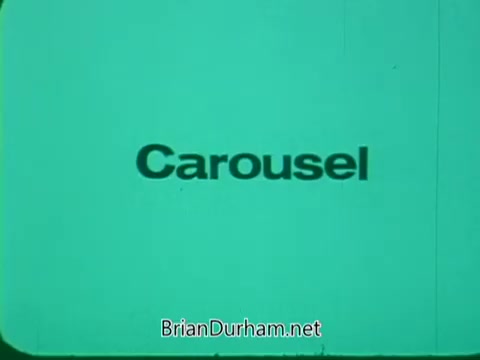The still features the word 'Carousel' displayed prominently against a solid turquoise background. The text is in a bold, clear font, suggesting a focus on clarity and emphasis, likely intended to capture the viewer's attention in the context of a promotional piece for the Pittsburgh Symphony's Promenades.