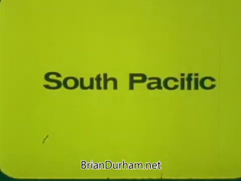 The still from the 'Pittsburgh Symphony Promenades Commercial' features a bright yellow background with bold black text displaying the title 'South Pacific.' The simplistic design focuses on the title, possibly indicating a theme or featured piece related to the Pittsburgh Symphony's programming.