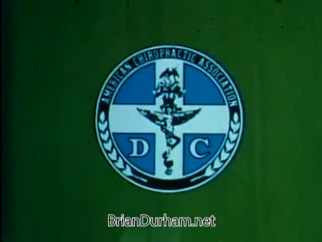 The still features the logo of the American Chiropractic Association set against a green background. The emblem includes elements such as a caduceus, which symbolizes healthcare, along with the letters 'D.C.' prominently displayed. The overall design reflects a professional image associated with chiropractic care. This PSA from 1967 likely aimed to promote awareness and understanding of chiropractic practices.