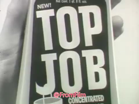 The still from the 'Top Job cleaner (with ammonia!)' commercial features a prominent product label for Top Job, highlighting it as a new and concentrated cleaner from Procter and Gamble. The design is bold and visually striking, with a focus on the product's name and its cleaning capabilities. The context includes a conversation between a woman and a man discussing the dullness of a light floor and introducing Top Job as a solution. The voice-over emphasizes its effectiveness, promising bright, clean results.