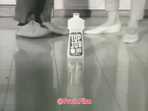 The still from the 'Top Job Cleaner (with ammonia!)' commercial features two pairs of feet—one in slippers and the other in shoes—standing on a shiny, clean floor. In the center is a bottle of Top Job cleaner, prominently displaying its label. The scene conveys a discussion about the appearance of the floor and highlights the product as an effective solution for keeping floors bright and clean. The playful tone and enthusiastic voice-over suggest excitement about the new product from Procter and Gamble.