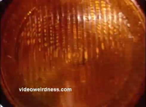 The still features a close-up of an orange light, likely a warning or indicator light. The texture is visible, highlighting its reflective surface and geometric patterns. The overall tone is warm, aligning with themes of alertness and safety typical in a Red Cross PSA.