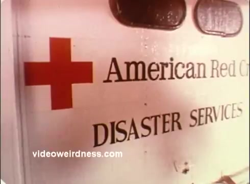 The still features a close-up of an ambulance or service vehicle, prominently displaying the emblematic red cross alongside the text 'American Red Cross' and 'DISASTER SERVICES.' The setting conveys a focus on emergency response and aid provided by the organization. The overall tone suggests preparedness and support during crises.